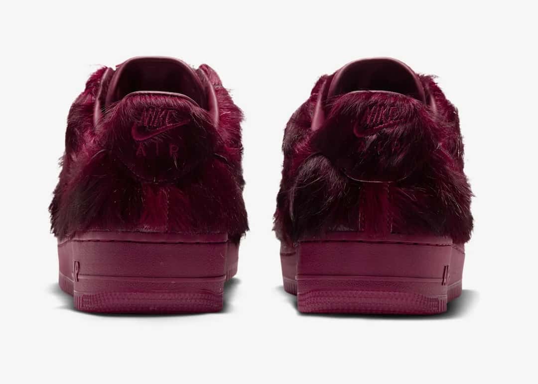 Talones del Nike Air Force 1 Low Pony Hair Team Red sobre fondo gris claro, con el bordado Nike Air medio tapado por el pelo bordó y la suela del mismo color