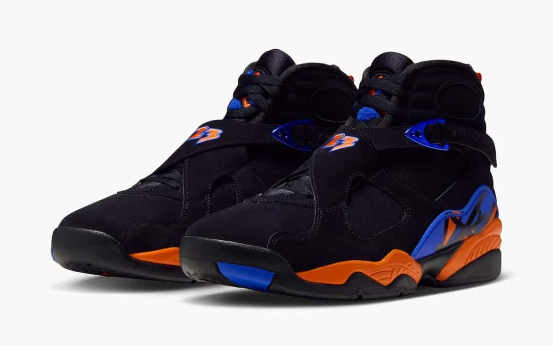 Par de Air Jordan 8 Knicks en negro con entresuela naranja y detalles azules, visto en diagonal sobre fondo blanco