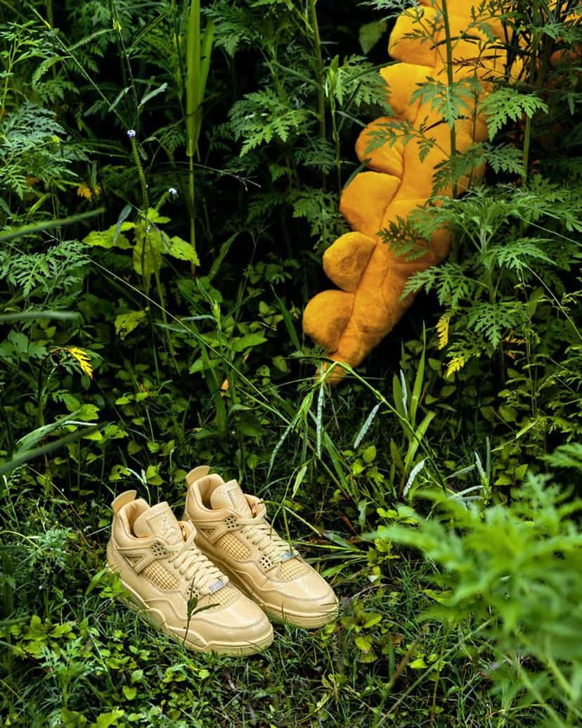 J Balvin x Air Jordan 4 Amazonas en medio de la vegetación, con una figura de peluche amarillo de fondo