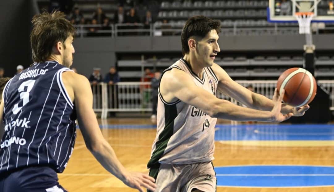 Un jugador de Gimnasia de Comodoro con la camiseta 14 da un pase ante la marca de un rival con camiseta azul a rayas