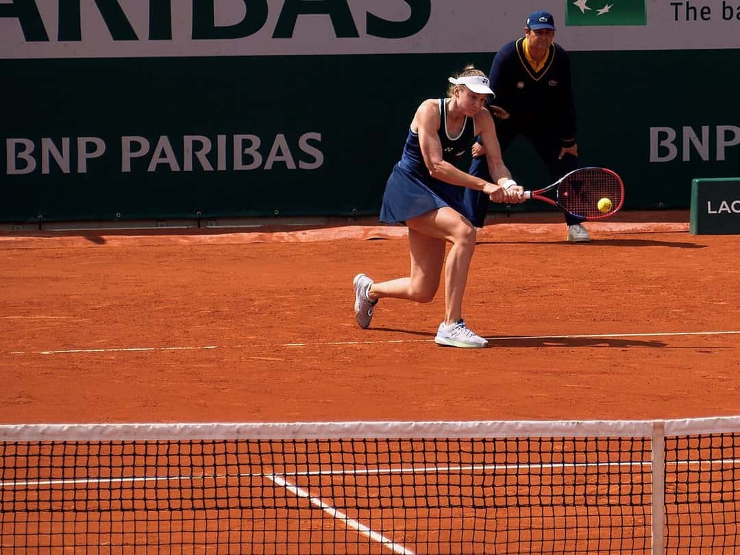 Foto de archivo: Elena Rybakina, de vestido azul y visera blanca, le pega un revés a dos manos en una cancha de polvo de ladrillo
