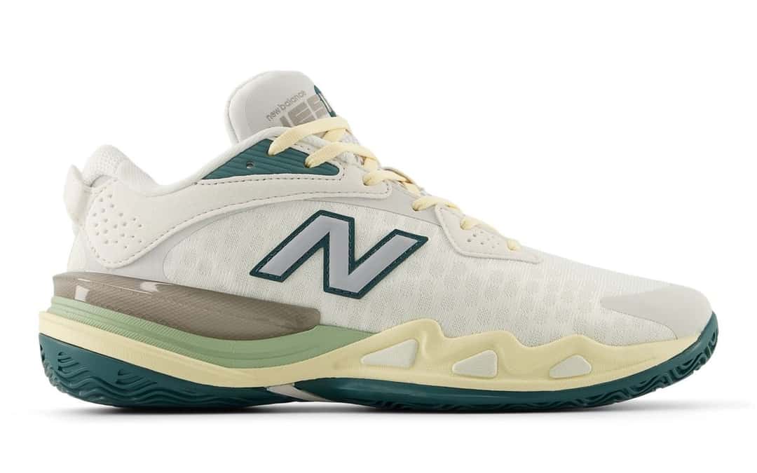 Zapatilla New Balance Hesi Low v2 de Cooper Flagg vista de costado sobre fondo blanco, con capellada blanca de malla, N plateada con borde verde petróleo, cordones amarillo pálido, mediasuela crema con franja verde clara y suela verde petróleo; foto de archivo
