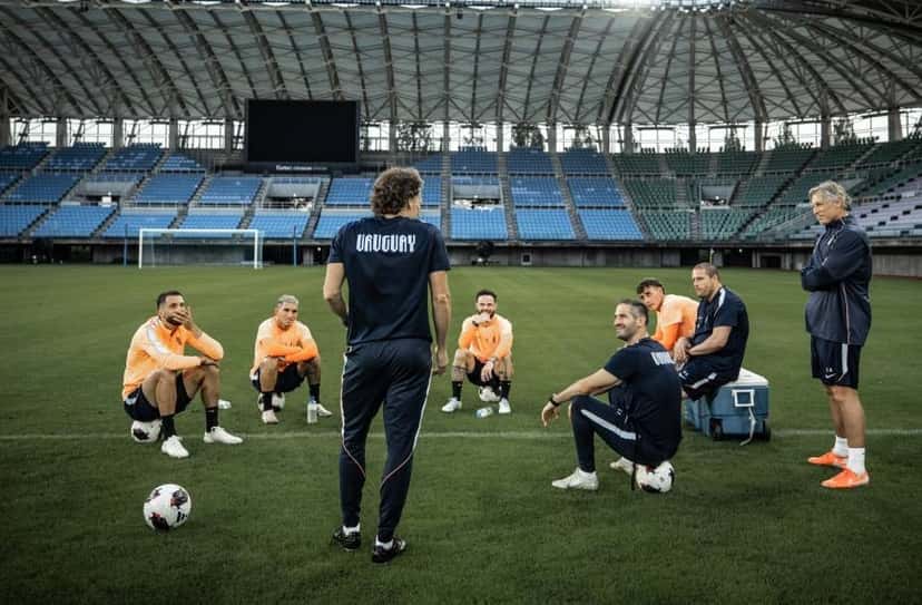 Diego Forlán, de espaldas con la ropa de entrenamiento de Uruguay, les habla a sus jugadores sentados sobre pelotas en un estadio techado de Japón. Foto de archivo de septiembre de 2026, difundida por la AUF
