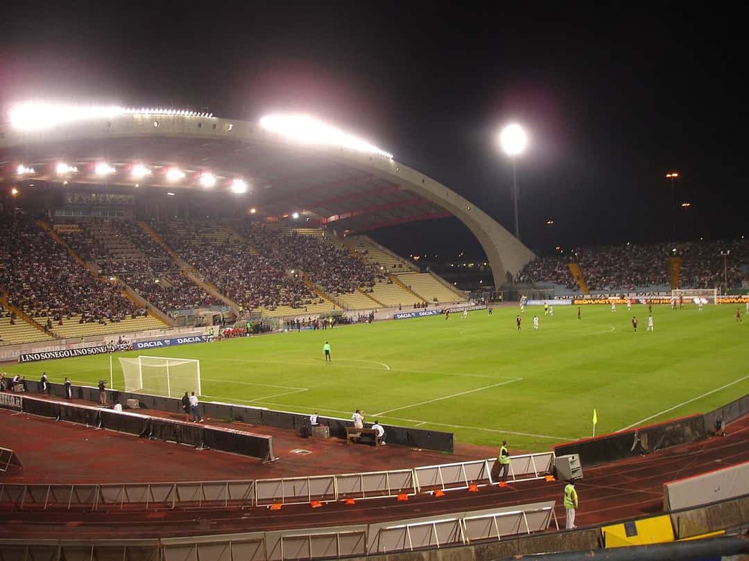 El estadio Friuli de Udine de noche, con la tribuna principal bajo su gran arco y la cancha iluminada durante un partido; foto de archivo de septiembre de 2009, dominio público, Wikimedia Commons
