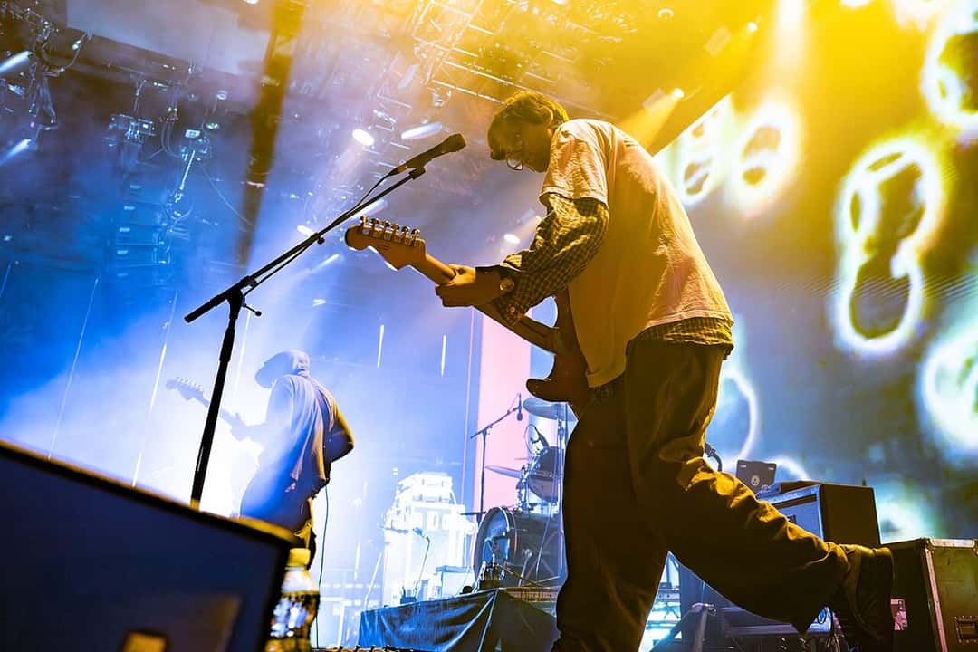 DIIV en vivo: un guitarrista toca de perfil frente al micrófono, con luces amarillas y azules y pantallas con imágenes detrás, en septiembre de 2025 (foto de archivo). Foto: DavidPMaynard, CC BY-SA 4.0, vía Wikimedia Commons