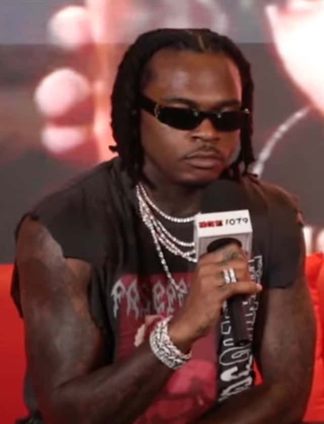 Gunna en junio de 2025, foto de archivo: con anteojos de sol negros, trenzas, cadenas y pulsera plateadas y una remera negra gastada, sosteniendo un micrófono. Foto: HOTSPOTATL, vía Wikimedia Commons (CC BY 3.0)