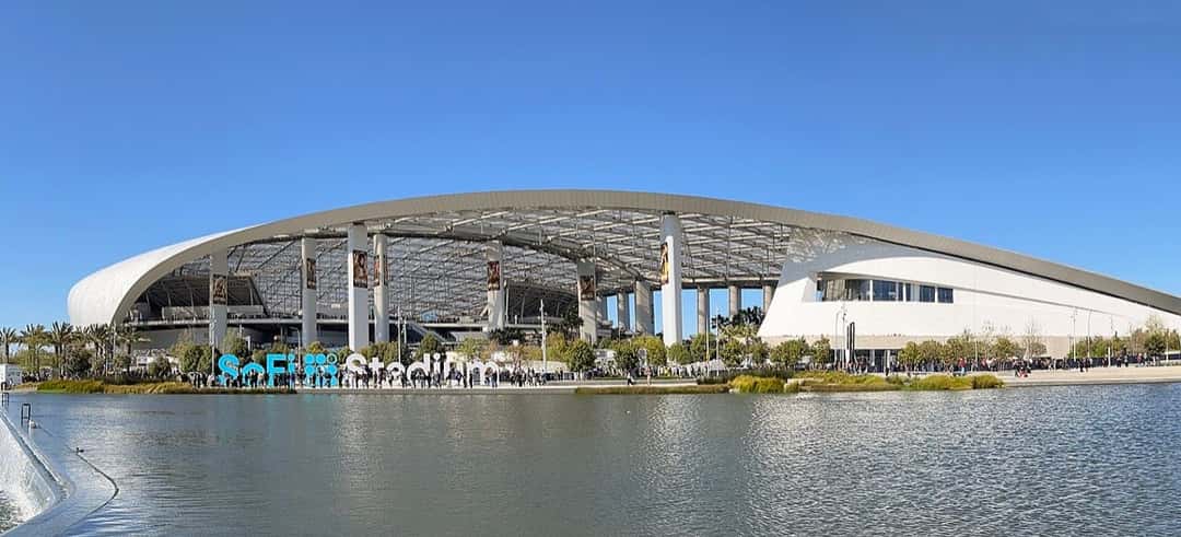 Vista exterior del SoFi Stadium de Inglewood, con su techo blanco curvo reflejado en el lago que rodea el estadio. Foto: Troutfarm27, CC BY-SA 4.0, vía Wikimedia Commons