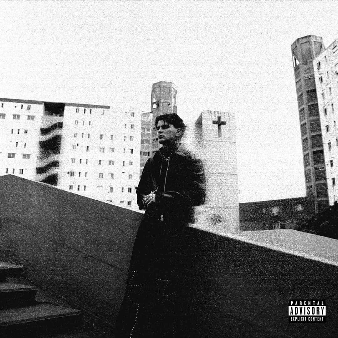 Portada de «NADIE-SABE», de LIT killah: foto en blanco y negro del músico, con campera oscura, apoyado en una baranda de cemento frente a edificios altos y una pared con una cruz