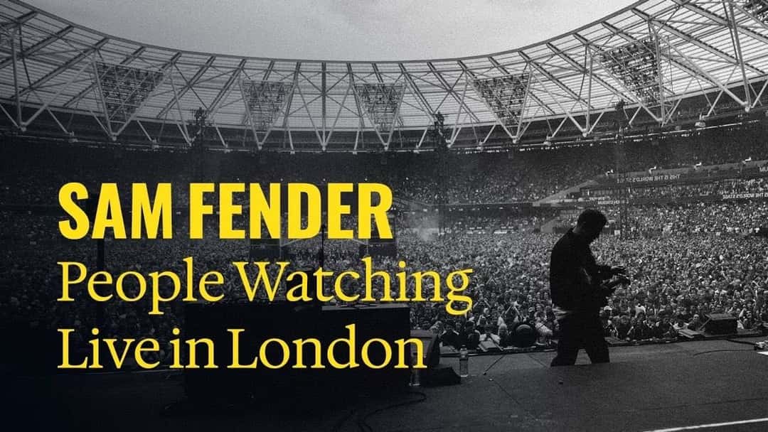 Placa del video oficial de «People Watching (Live in London)», de Sam Fender: el músico de espaldas con la guitarra frente a un estadio lleno, con el título en letras amarillas (fotograma del video oficial)