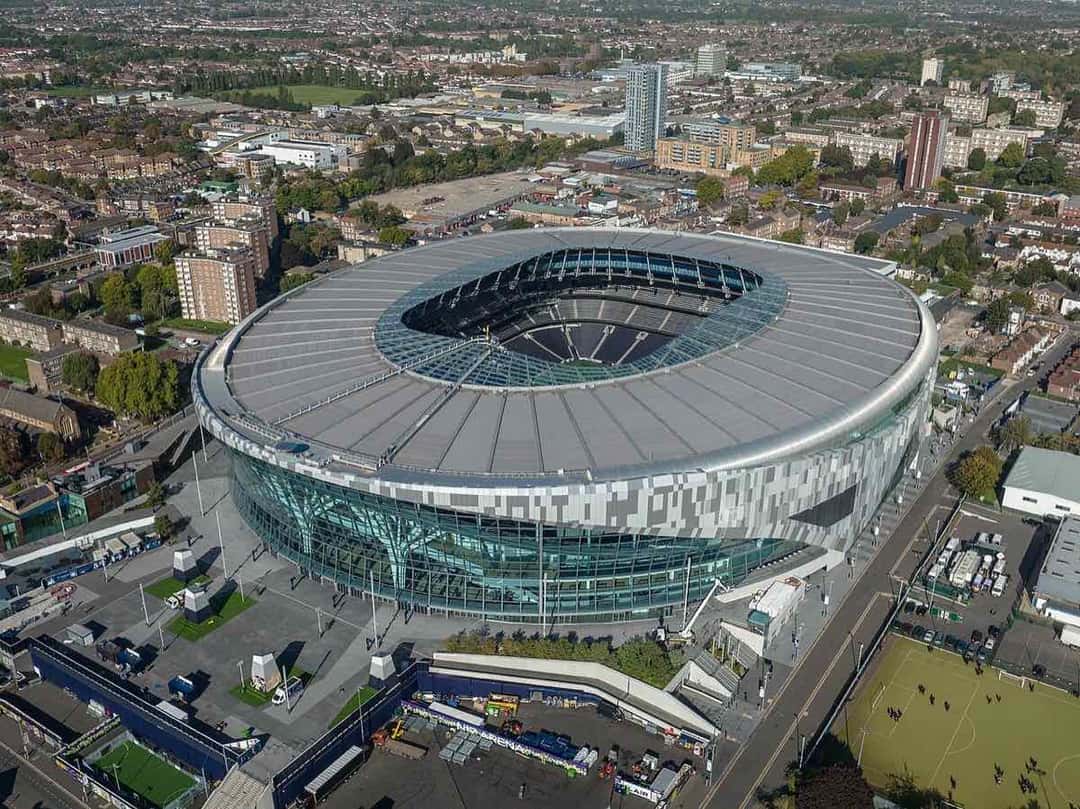 Vista aérea del Tottenham Hotspur Stadium de Londres, con su techo plateado y su fachada de vidrio, rodeado de casas y edificios del norte de la ciudad, en octubre de 2022 (imagen del lugar del show). Foto: Arne Müseler, CC BY-SA 3.0 DE, vía Wikimedia Commons