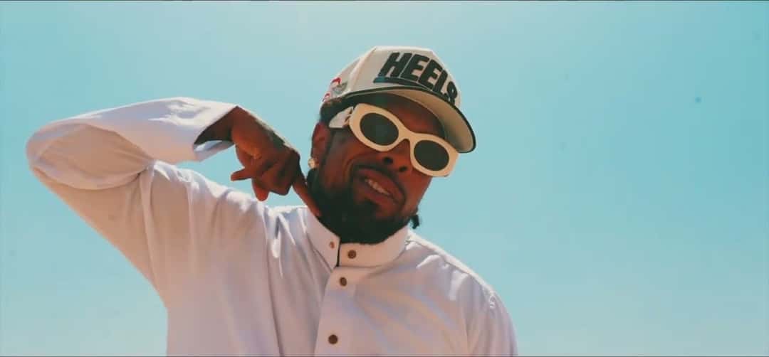 Westside Gunn con gorra blanca, anteojos de sol blancos y camisa blanca, en una escena del video oficial de «ZILLA»