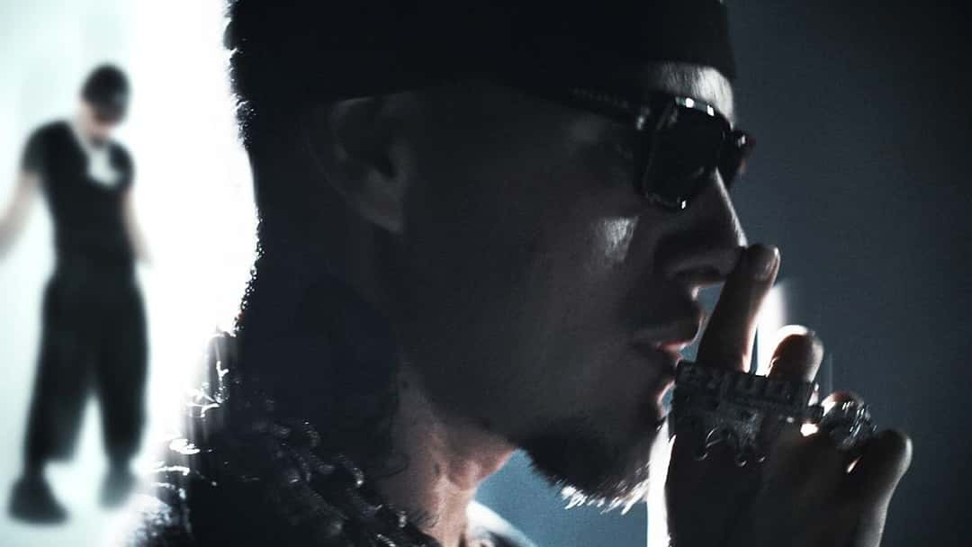 Fotograma de archivo del video oficial de «ON NOTHING»: Yeat, con anteojos oscuros, gorro y anillos, se lleva la mano a la cara en primer plano, mientras atrás aparece su silueta a contraluz