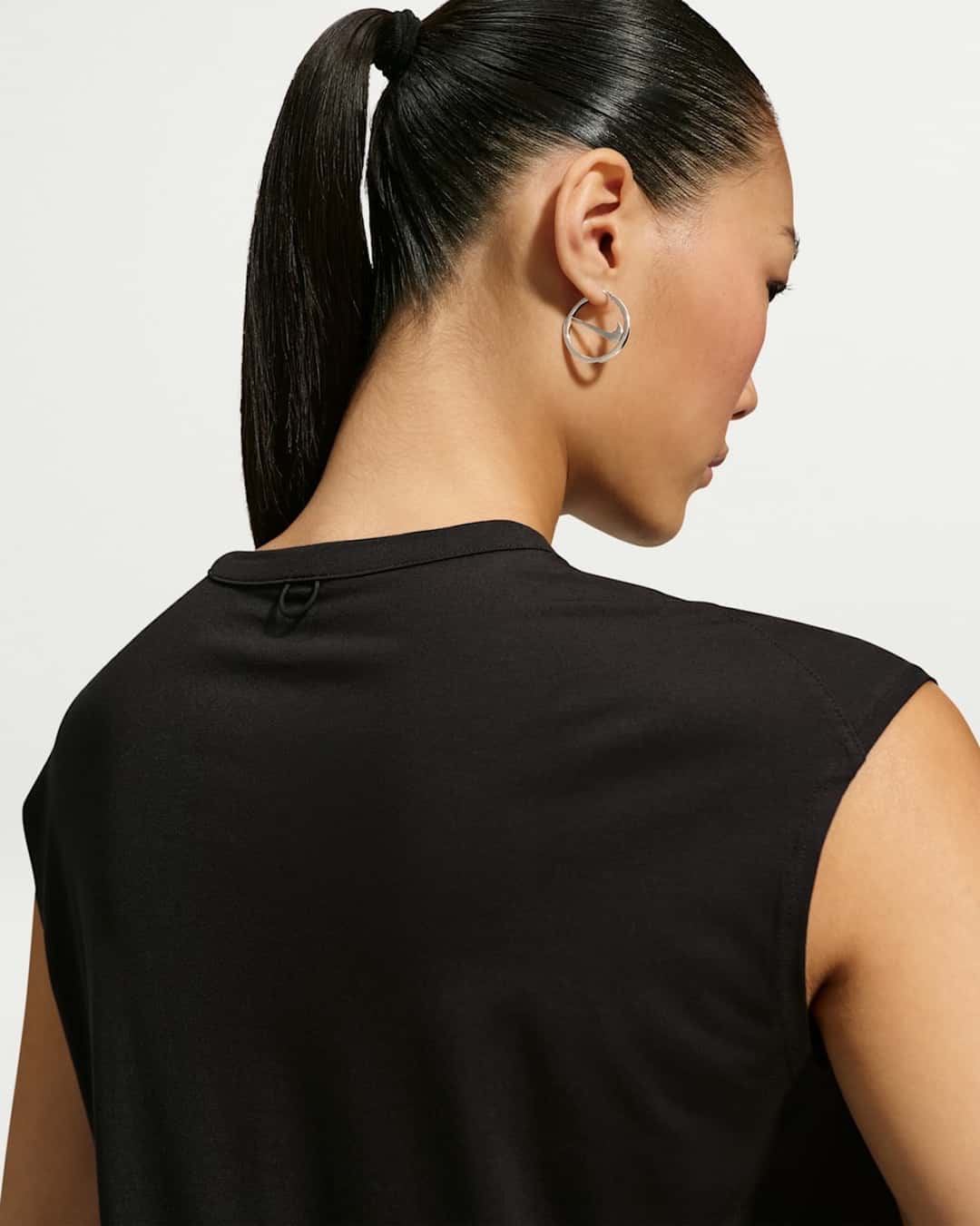 Mujer de espaldas con el pelo atado y remera negra sin mangas, usando una argolla plateada de la colección de joyería de Nike con el Swoosh integrado al aro