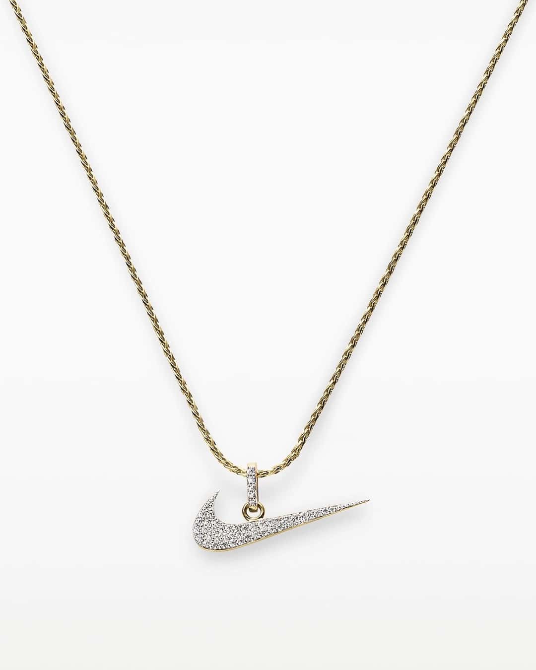 Collar Swoosh pavé de Nike sobre fondo blanco, con un Swoosh dorado cubierto de pequeñas piedras transparentes colgando de una cadena trenzada dorada