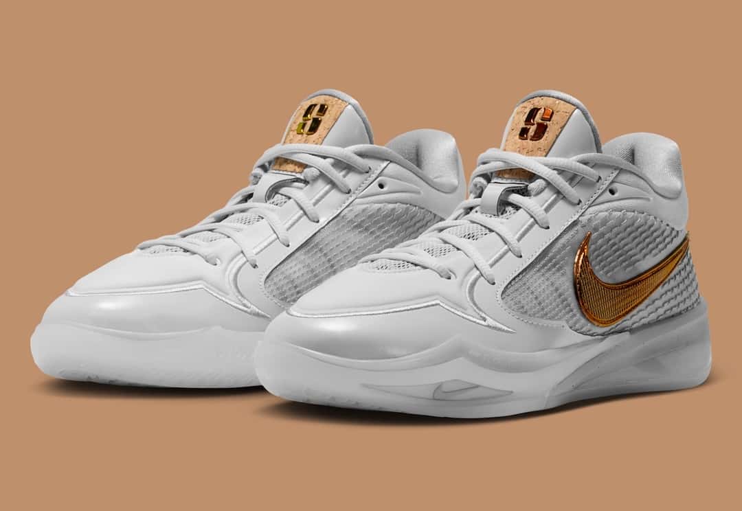 Par de Nike Sabrina 4 Cork en vista tres cuartos, blancas con el Swoosh dorado y la S de corcho en las lengüetas, sobre fondo color caramelo