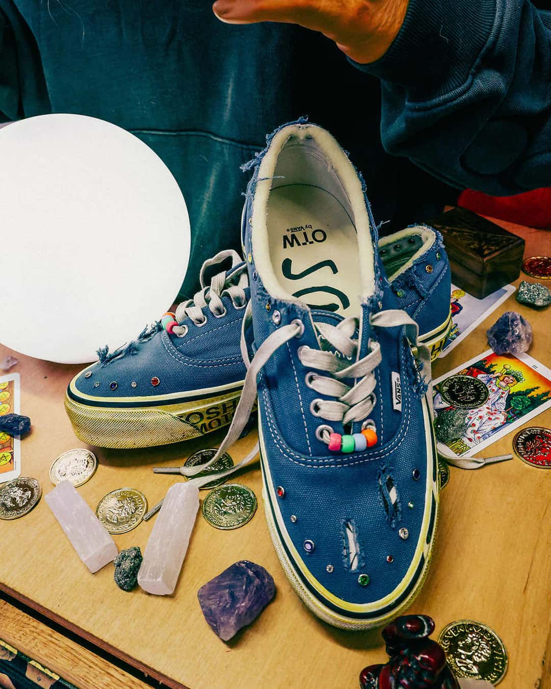Par de Satoshi Nakamoto x Vans Era 95 Lucky Charms azul con roturas en la puntera, joyas de colores y cuentas en los cordones, rodeado de cristales, monedas y cartas de tarot