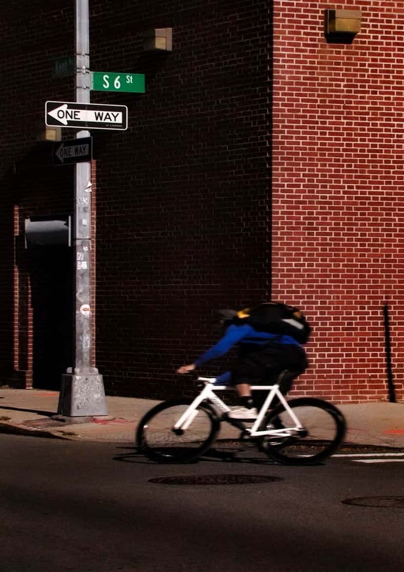 Un mensajero en bicicleta blanca dobla una esquina de ladrillo bajo el cartel de una calle de Nueva York. Foto: Sébastien Lorsbach y Julien Caldarone para Salomon
