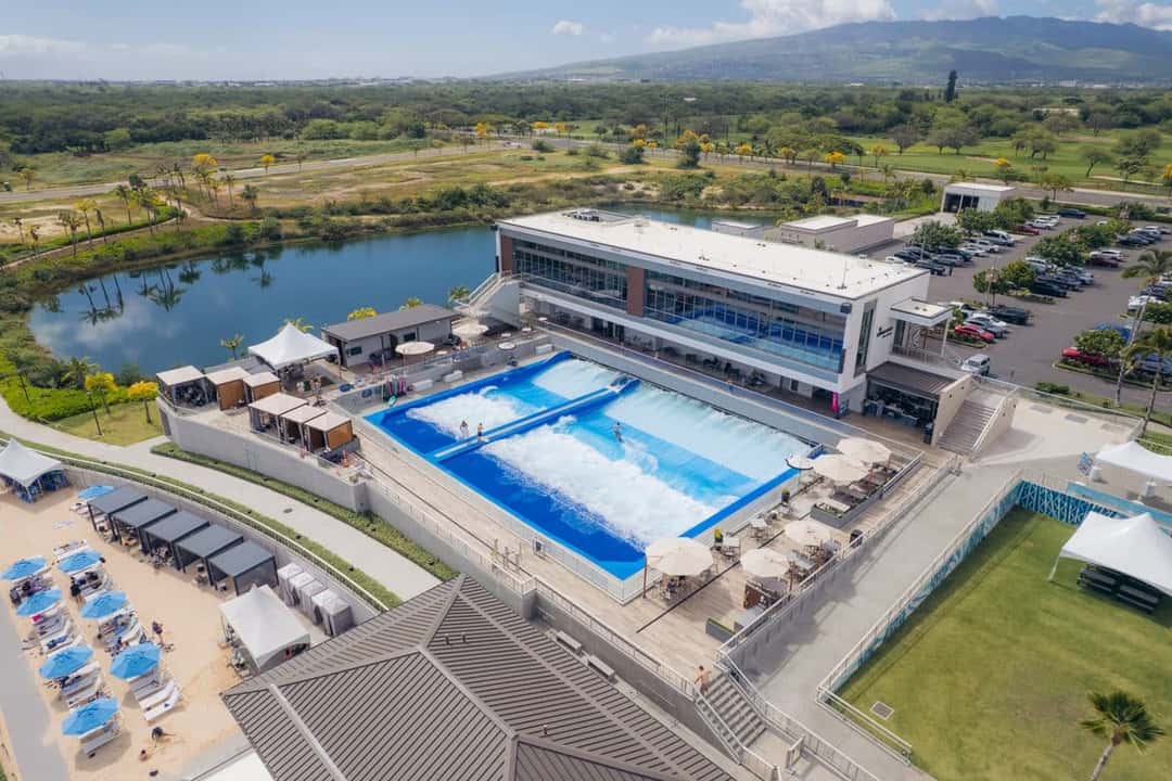 Vista aérea del complejo Wai Kai, en Ewa Beach: la pileta de la ola artificial junto a un edificio, una laguna y las montañas de Oahu de fondo