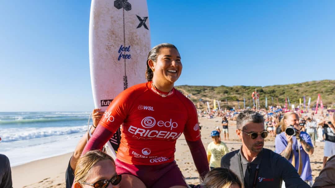 Brisa Hennessy, con la lycra roja del EDP Ericeira Pro, sonríe llevada en andas por la arena de Ribeira d'Ilhas, con su tabla detrás y público en la playa