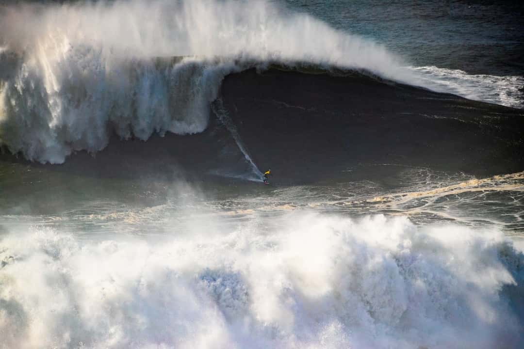 Foto de archivo: Laura Crane, con traje amarillo, baja una ola gigante mientras la espuma de la rompiente explota a su izquierda en Praia do Norte