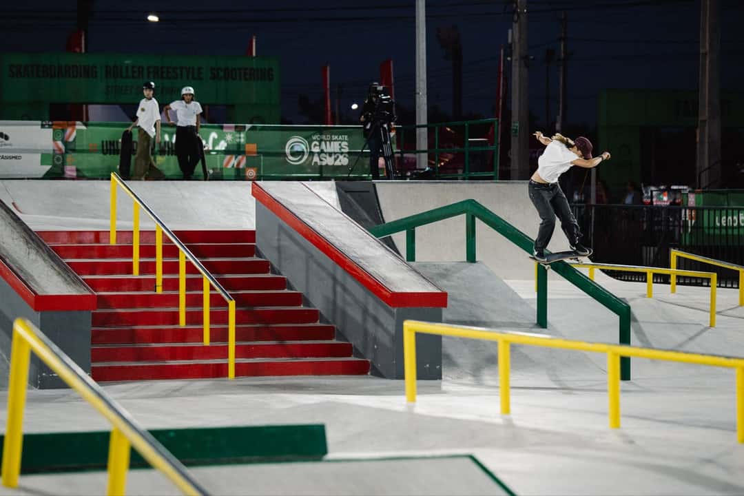 Flic Turner, con remera blanca, se desliza sobre una baranda amarilla de la pista de street de Luque de noche, con el cartel de los World Skate Games Asunción 2026 detrás