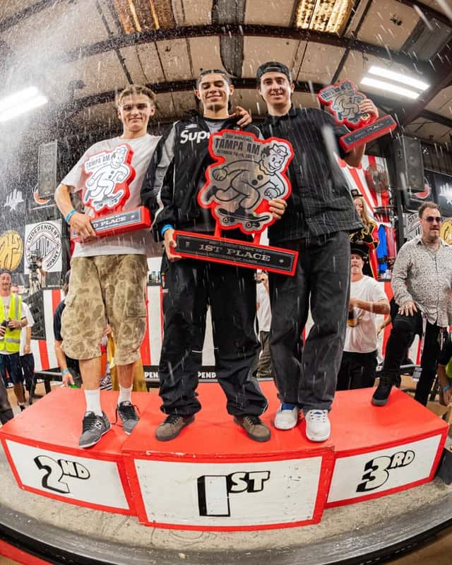 Abner Pietro sostiene el trofeo de primer puesto en el centro del podio del Tampa Am 2025, con Rocco Müller a su izquierda y Chris Setinas a su derecha