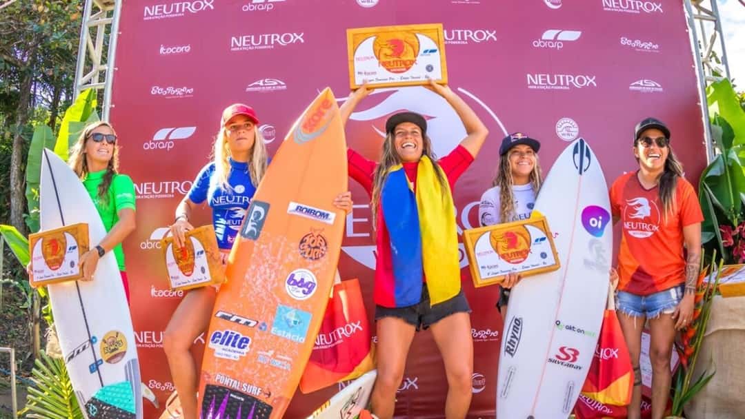 Mimi Barona, con una bandera de Ecuador sobre los hombros, levanta el trofeo en lo más alto del podio entre otras cuatro surfistas (foto de archivo)