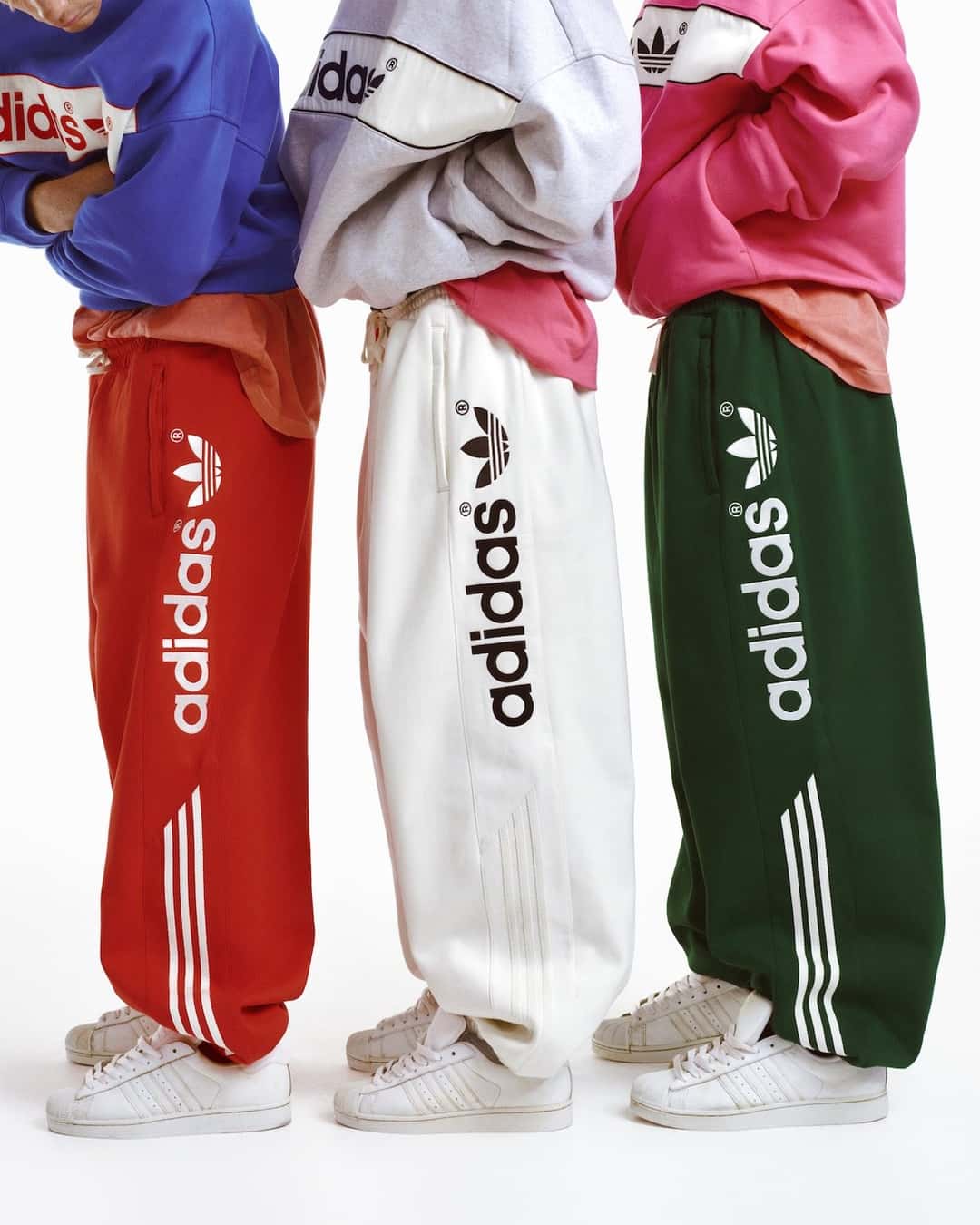 Tres joggings de adiSignature en rojo, blanco y verde con la palabra adidas y el Trébol a lo largo de la pierna