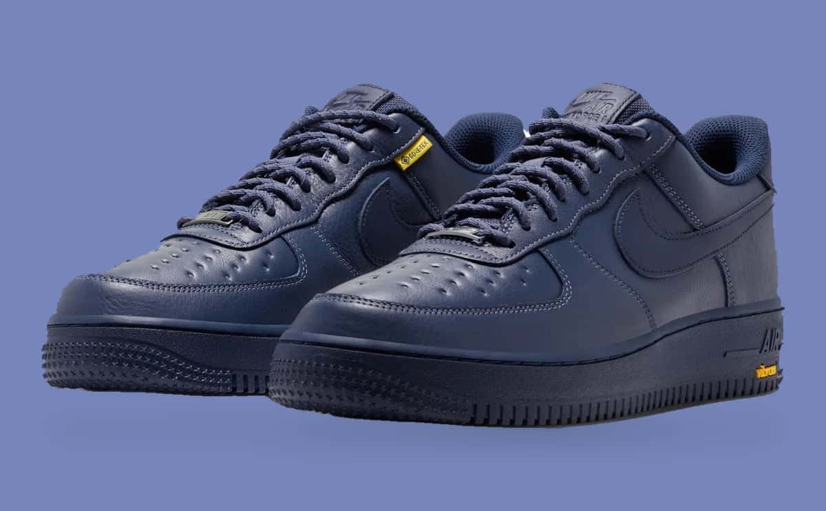Par de Nike Air Force 1 Low GORE-TEX Thunder Blue en azul marino entero, con hoyuelos en la puntera, cordones al tono y logo Vibram amarillo en la suela, sobre fondo celeste