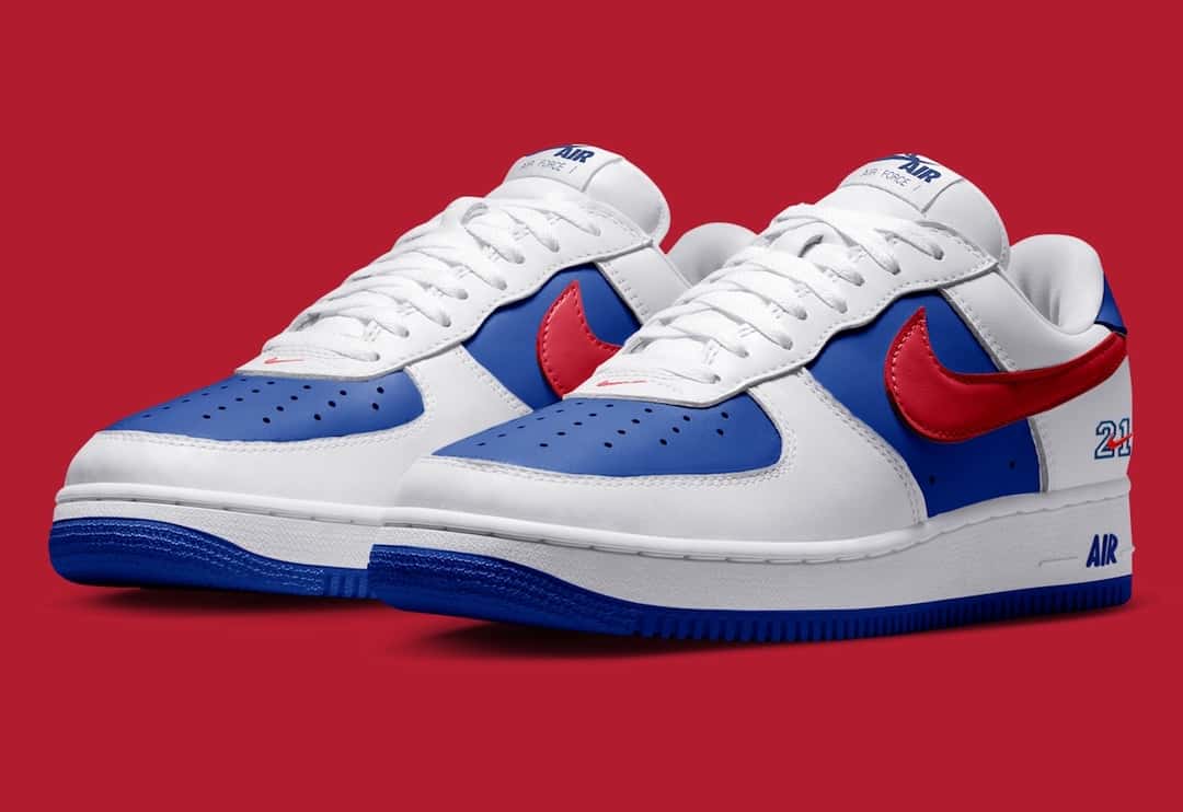 Par de Nike Air Force 1 '01 Philly sobre fondo rojo, en vista tres cuartos, con cuero blanco, paneles azules, Swoosh rojo y suela azul