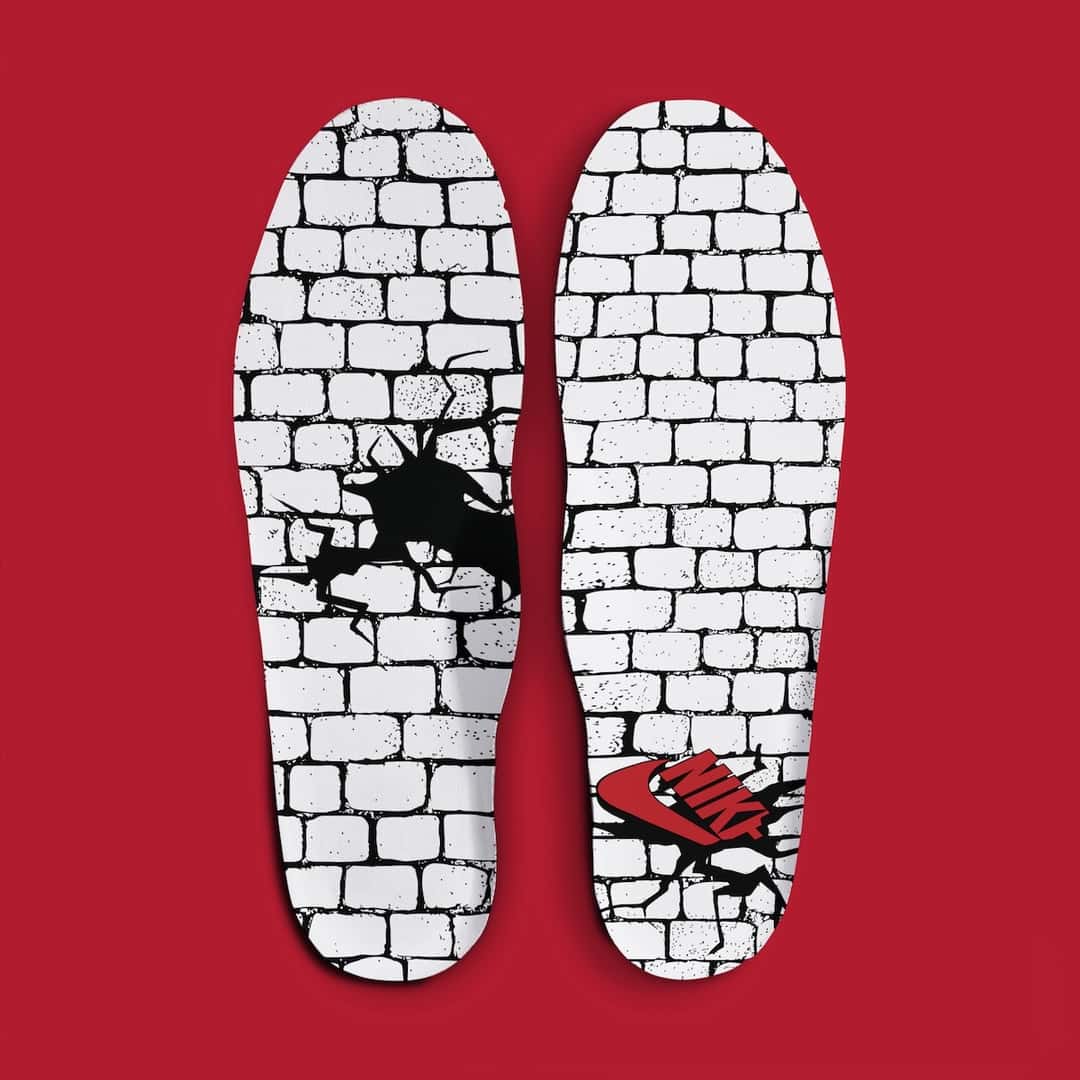 Plantillas de la Nike Air Force 1 '01 Philly sobre fondo rojo, con dibujo de pared de ladrillos blancos, una rajadura negra y el logo de Nike en rojo saliendo de la pared