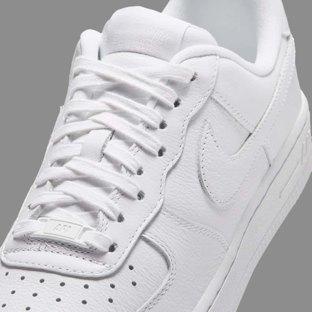Detalle de la Nike Air Force 1 Low de punta cuadrada Triple White, con el cuero graneado, los cordones blancos y el Swoosh del mismo color