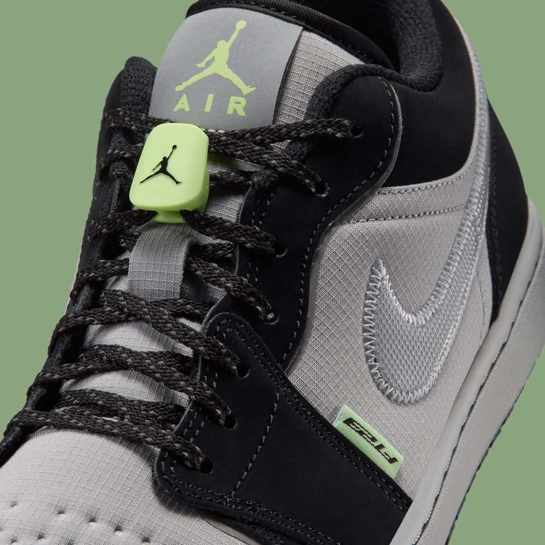 Detalle del Air Jordan 1 Low Light Smoke Grey Barely Volt con la traba de cordones verde flúor con el Jumpman, la lengüeta con el logo Jumpman Air en verde, los cordones negros tipo trekking y el Swoosh plateado cosido en zigzag sobre el ripstop