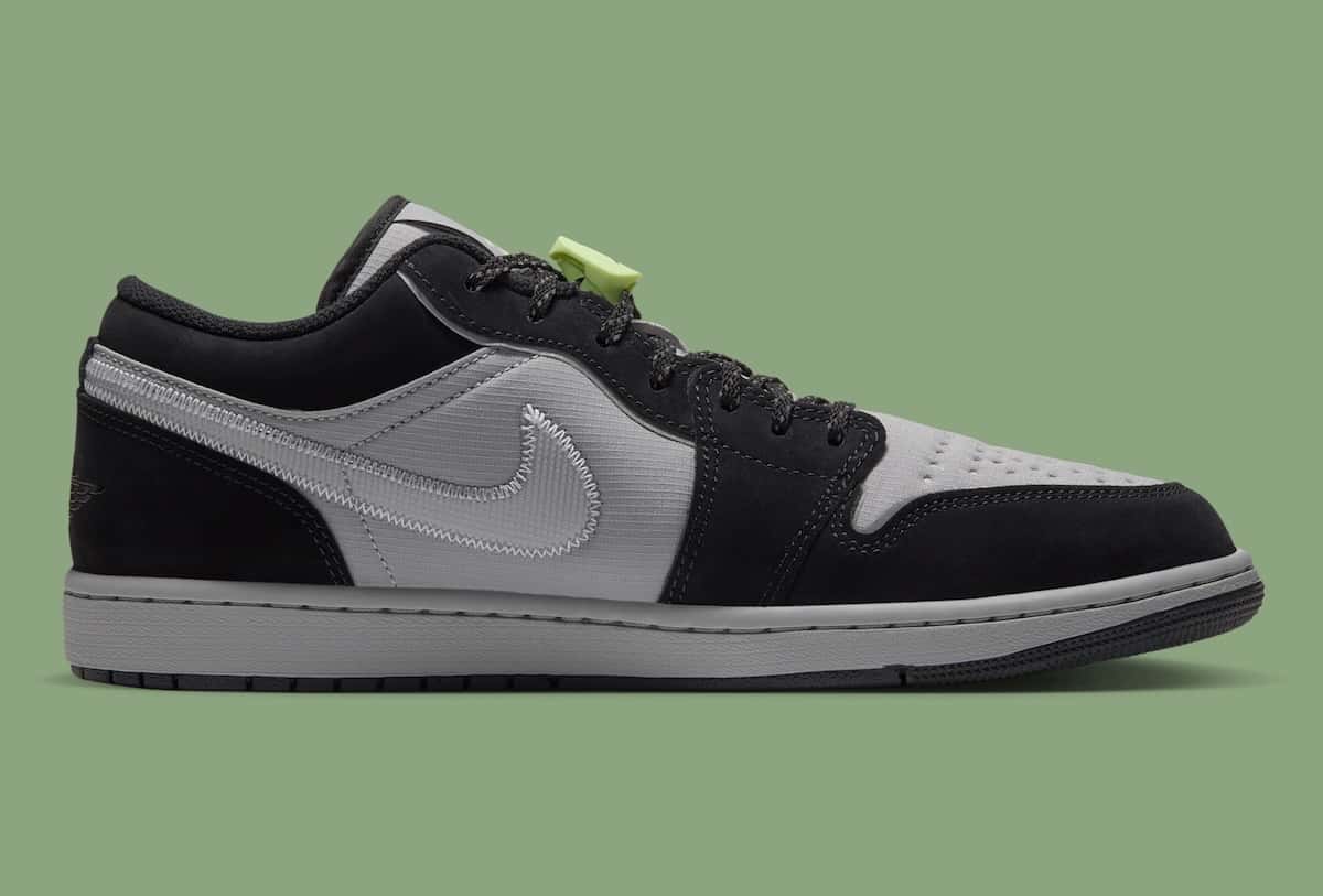 Air Jordan 1 Low Light Smoke Grey Barely Volt de perfil sobre fondo verde, con paneles de ripstop gris, gamuza negra alrededor de la puntera, en los ojales y el talón, Swoosh plateado reflectivo y traba de cordones verde flúor