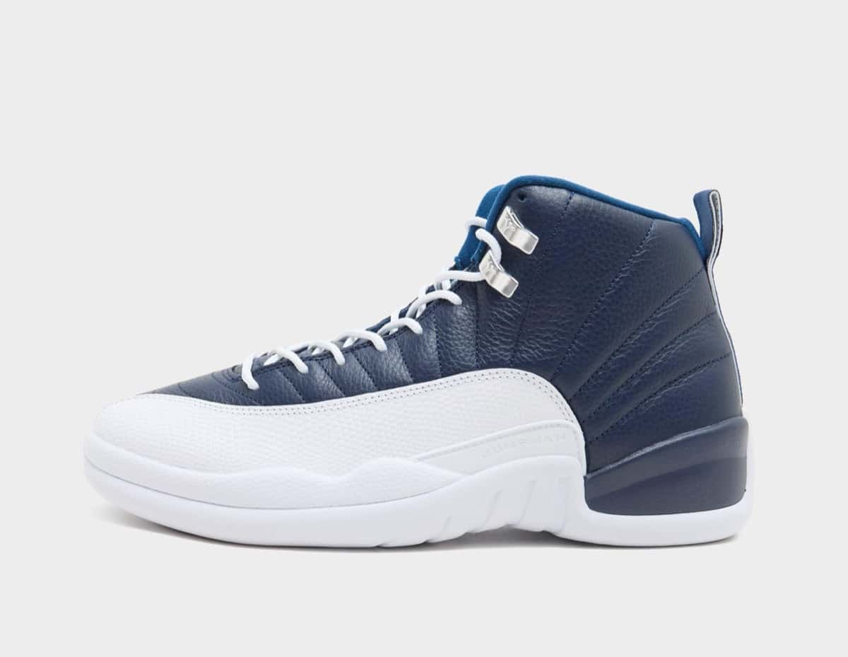 Air Jordan 12 Obsidian de perfil sobre fondo gris claro, con upper de cuero azul marino con costuras radiales, puntera y entresuela blancas, ganchos plateados en los cordones y forro azul francés en el cuello