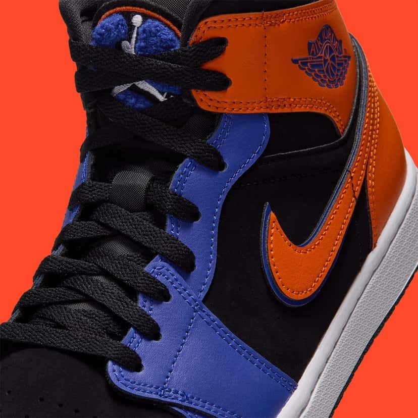 Detalle de la Air Jordan 1 Mid Knicks con el parche de chenille en la lengüeta, el logo Wings naranja en el tobillo y el Swoosh naranja