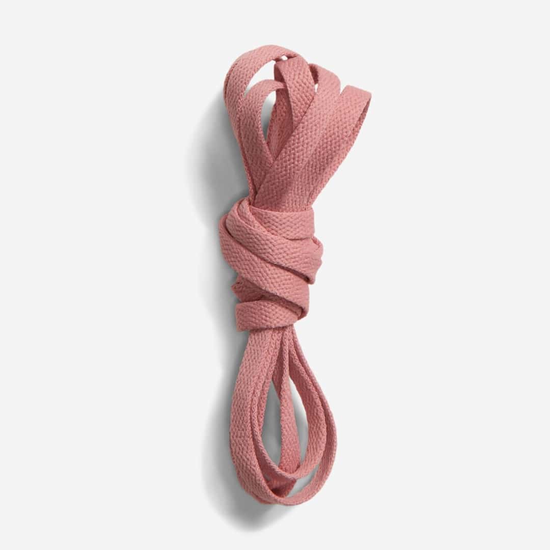Par de cordones planos de color rosa pálido enrollados, sobre fondo gris claro