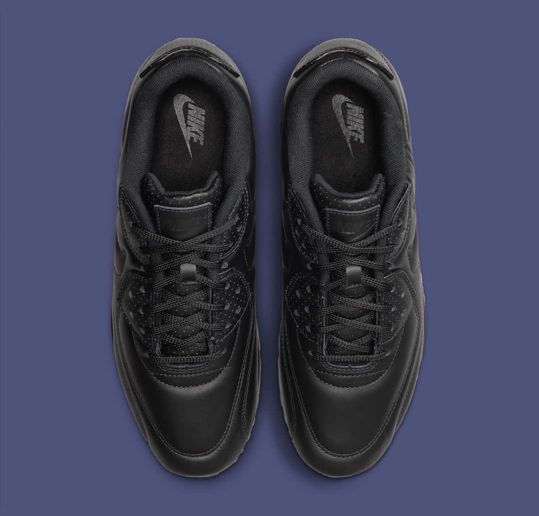 Par de Nike Air Max 90 SP Black Leather vistas desde arriba sobre fondo azul grisáceo, con cuero negro, pasacordones perforados y el logo de Nike en la lengüeta