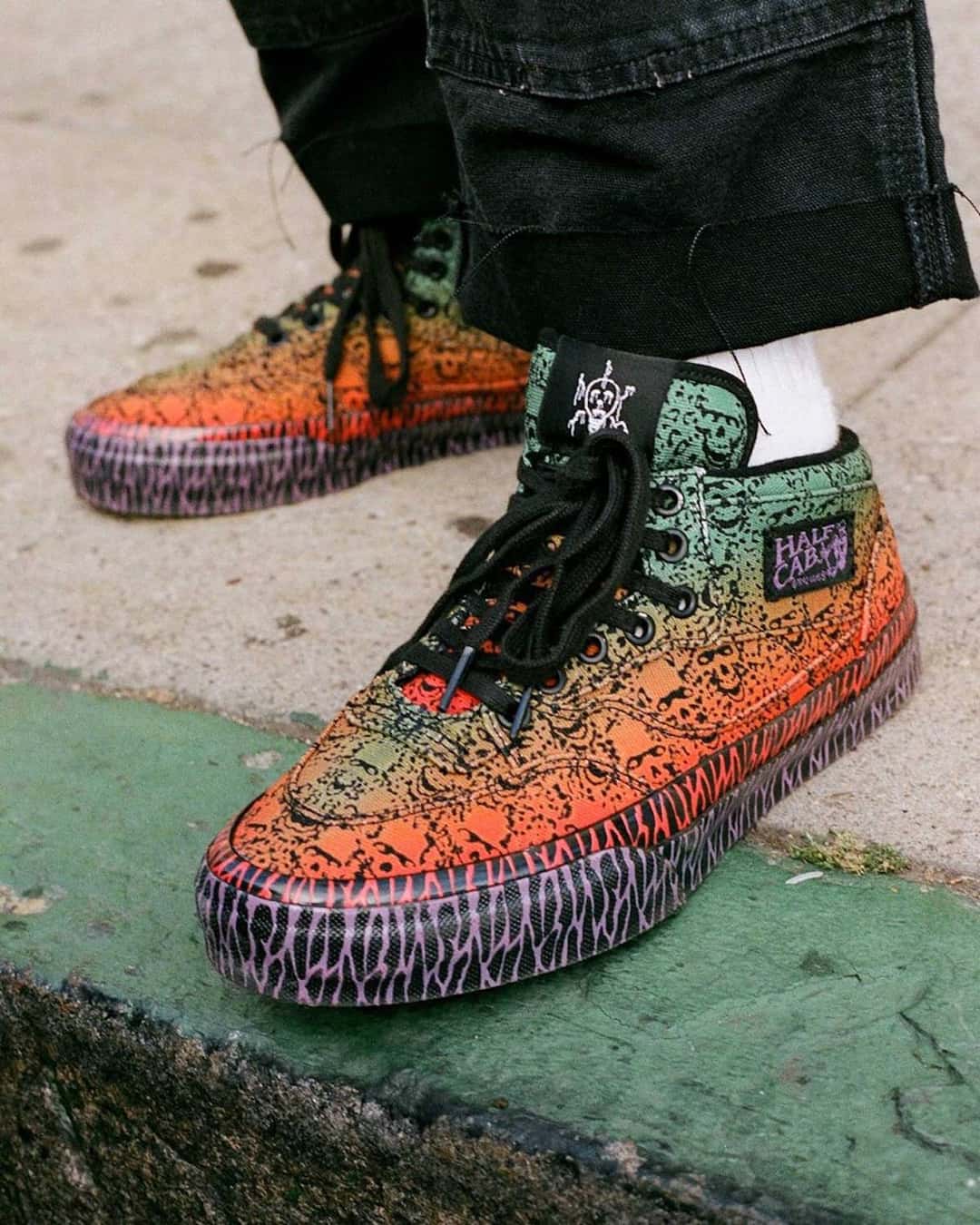 Bad Idea by Chito x Vans Half Cab 33 puesta, con jean negro y medias blancas, sobre un cordón de vereda pintado de verde