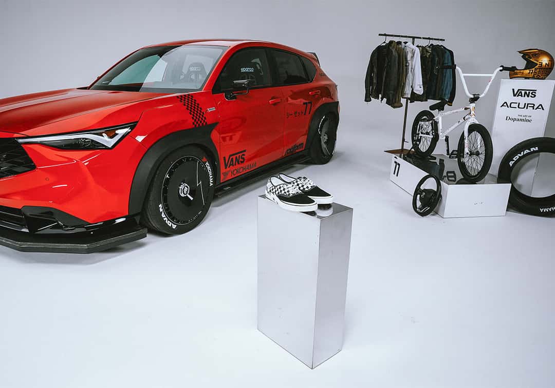 Exhibición de la collab de Vans y Coco Zurita con el Acura ADX rojo, el Authentic sobre un pedestal plateado, una bici de BMX blanca y un perchero con ropa