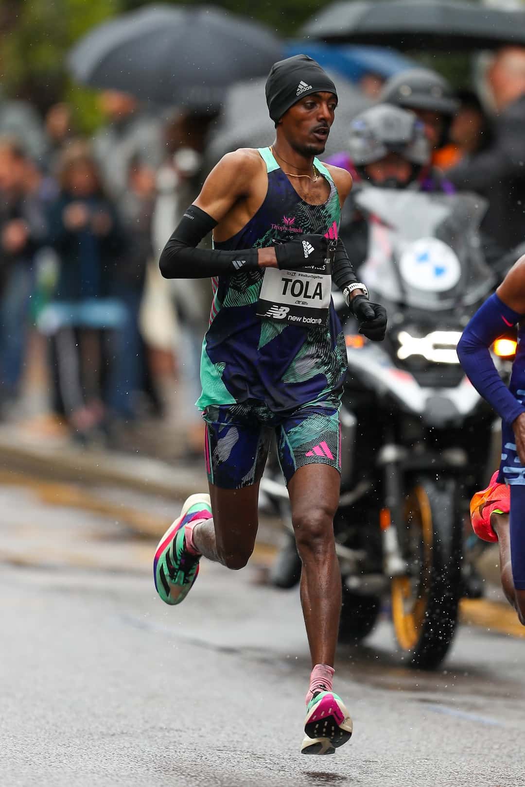 Foto de archivo: Tamirat Tola, con musculosa oscura, gorro negro y número con su apellido, corre bajo la lluvia en el Maratón de Londres 2023, seguido por una moto
