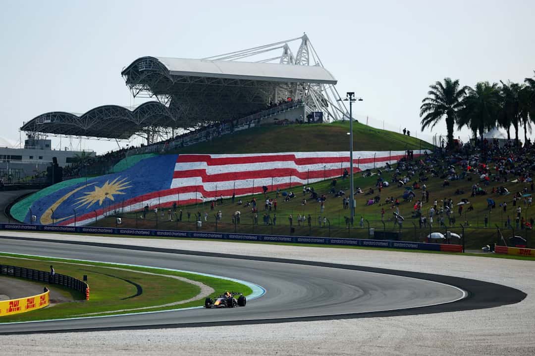 Un Red Bull dobla en Sepang frente a la tribuna principal, con la bandera de Malasia pintada en la colina