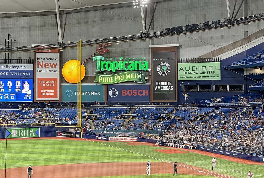 Foto de archivo: el jardín izquierdo de Tropicana Field, con el cartel luminoso de Tropicana y una naranja gigante sobre la tribuna, el poste de foul amarillo y los jugadores en el campo durante un partido de los Rays