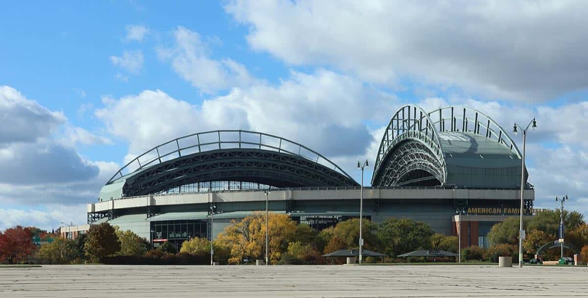 Imagen del estadio: el American Family Field de Milwaukee, con su techo de arcos metálicos, rodeado de árboles con colores de otoño