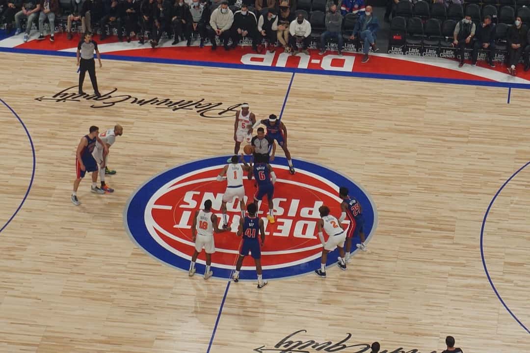 Foto de archivo: salto inicial en el círculo central del Little Caesars Arena, con el logo de los Detroit Pistons en el parquet y jugadores de los dos equipos alrededor