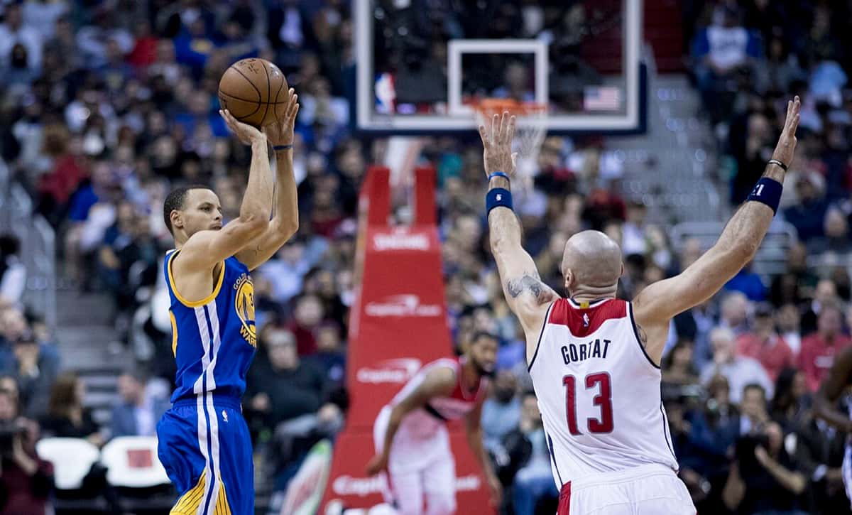 Foto de archivo: Stephen Curry, con la camiseta azul de los Warriors, lanza un tiro en suspensión ante la marca de un jugador de los Wizards, de blanco