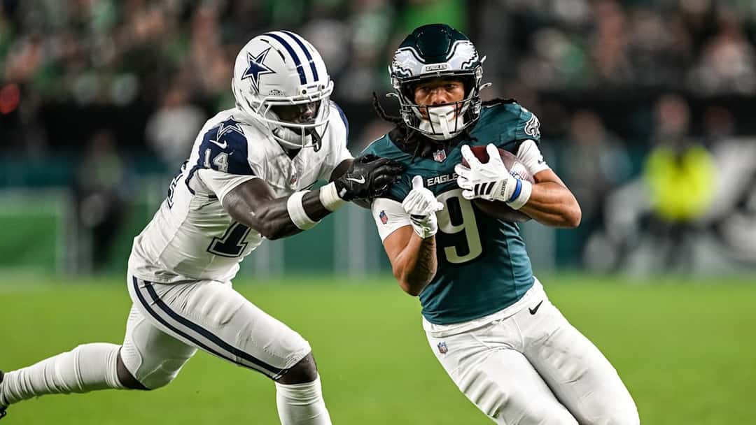 Makai Lemon, de los Eagles, con la camiseta verde número 9, corre con la pelota mientras lo agarra un defensor de los Cowboys de blanco número 14