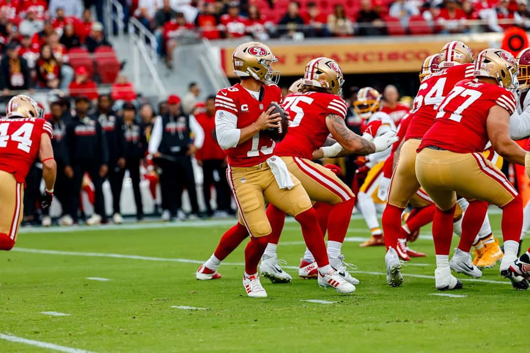 Brock Purdy, con la camiseta roja número 13, retrocede para lanzar protegido por su línea ofensiva ante los Commanders en el Levi's Stadium