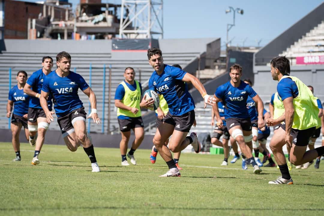 Foto de archivo: jugadores de Los Pumas, con remeras azules y pecheras amarillas, corren con la pelota en un entrenamiento en una cancha de pasto