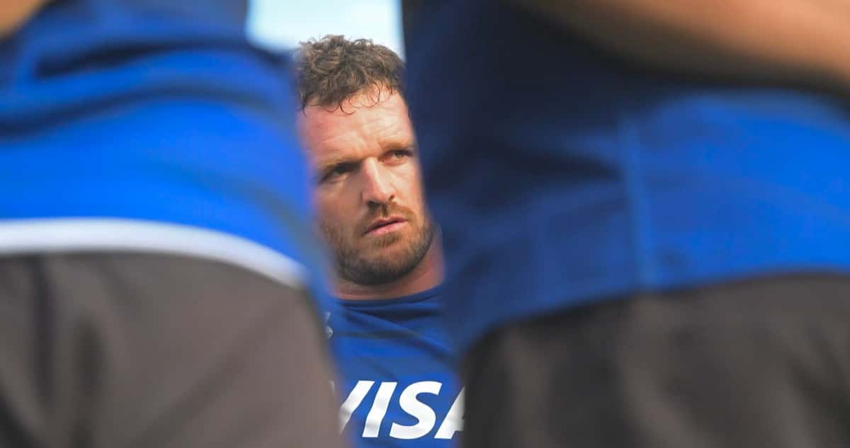 Foto de archivo: Julián Montoya, con la remera azul de entrenamiento de Los Pumas, escucha entre dos compañeros de espaldas durante una práctica